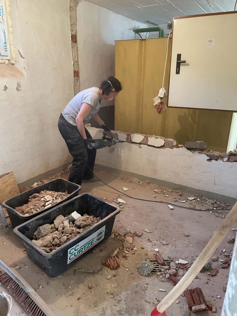 Ferienhaus Kellerwald Person beim Abriss einer Wand in einem Raum mit Baumulden Ferienhaus Edersee