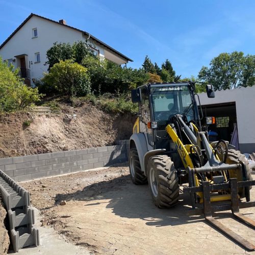 Ferienhaus Kellerwald Bagger auf einer Baustelle mit neuem Mauerwerk und einem Wohnhaus im Hintergrund Ferienhaus Edersee