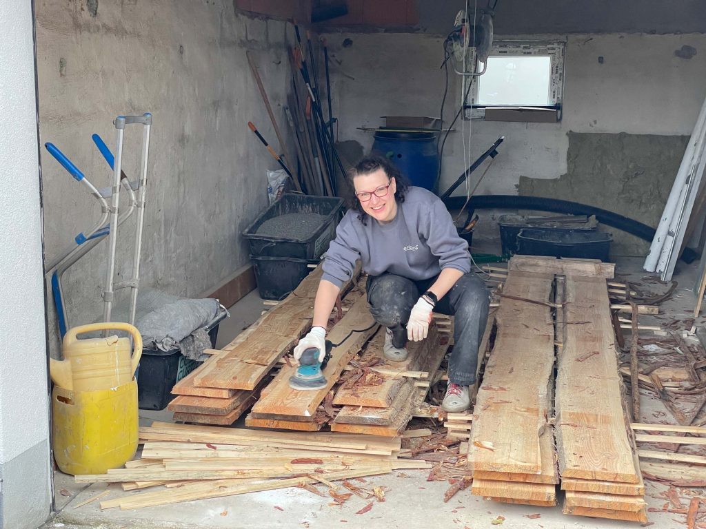 Ferienhaus Kellerwald Frau schleift Holzbretter in einer Werkstatt mit Werkzeugen um sie herum Ferienhaus Edersee, Ein Jahr voller Arbeit