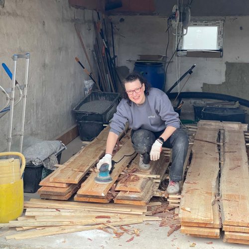 Ferienhaus Kellerwald Frau schleift Holzbretter in einer Werkstatt mit Werkzeugen um sie herum Ferienhaus Edersee, Ein Jahr voller Arbeit