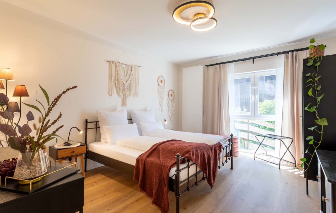 Moderne Schlafzimmer mit Doppelbett, Pflanzen und natürlichem Licht aus dem Fenster,