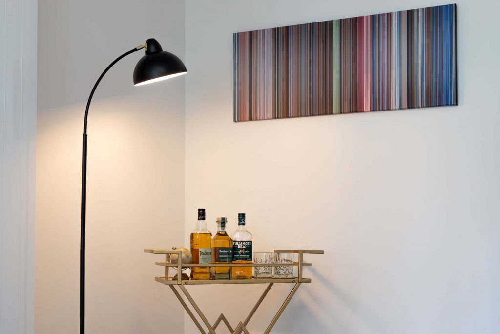Vacation home Kellerwald Modern floor lamp next to a golden bar cart with whiskey bottles and colorful wall art, vacation home Edersee, gallery