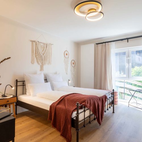 Modern bedroom with double bed, plants, and natural light from the window,