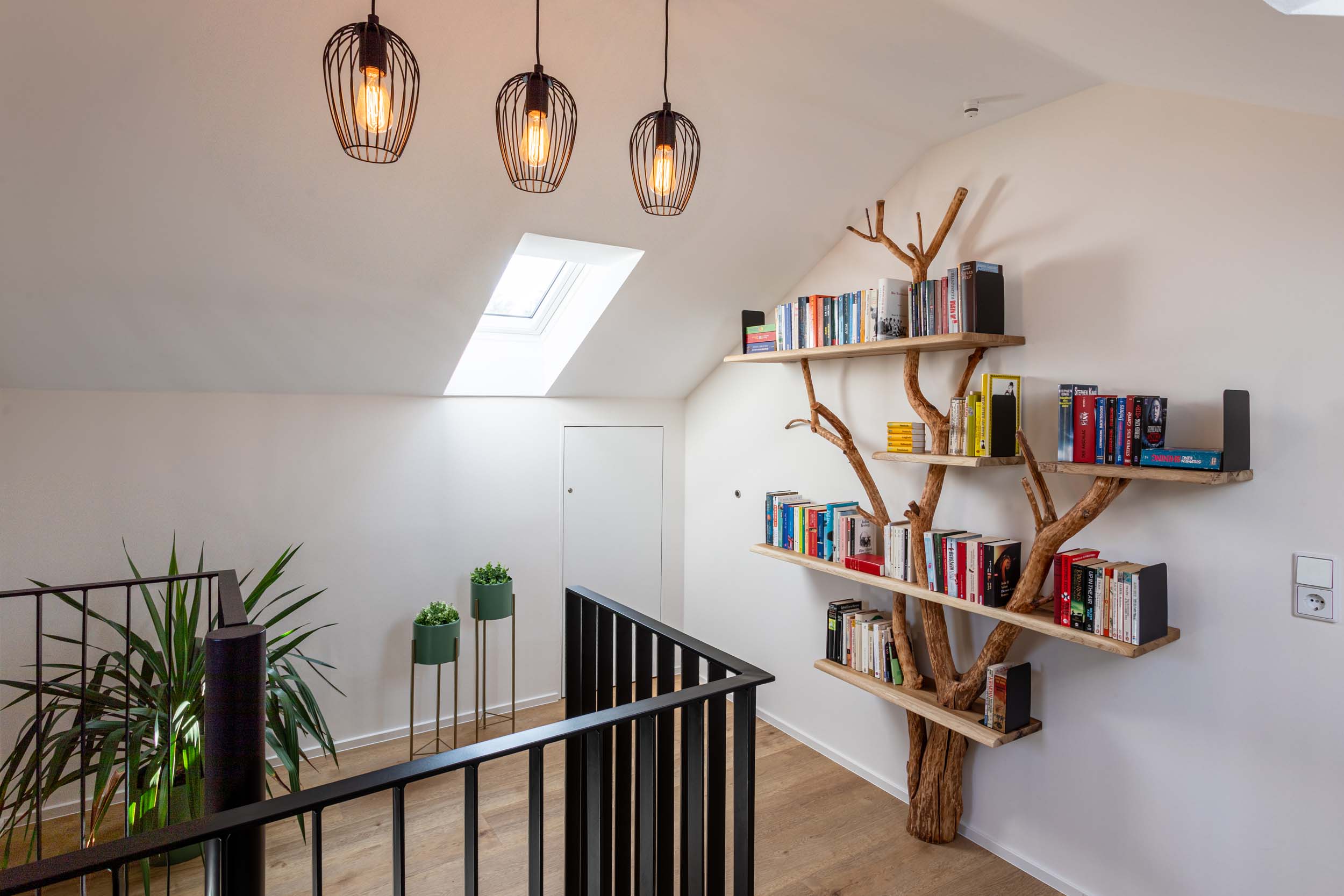 Ferienhaus Kellerwald Ein modernes Wohnzimmer mit einem Bücherregal in Baumform und stilvollen Deckenlampen Ferienhaus Edersee, Bücherträume