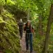 Ferienhaus Kellerwald Zwei Menschen wandern durch einen grünen, bewaldeten Pfad zwischen Bäumen und Moos Ferienhaus Edersee, Zertifizierung als „Qualitätsgastgeber – wanderbares deutschland“