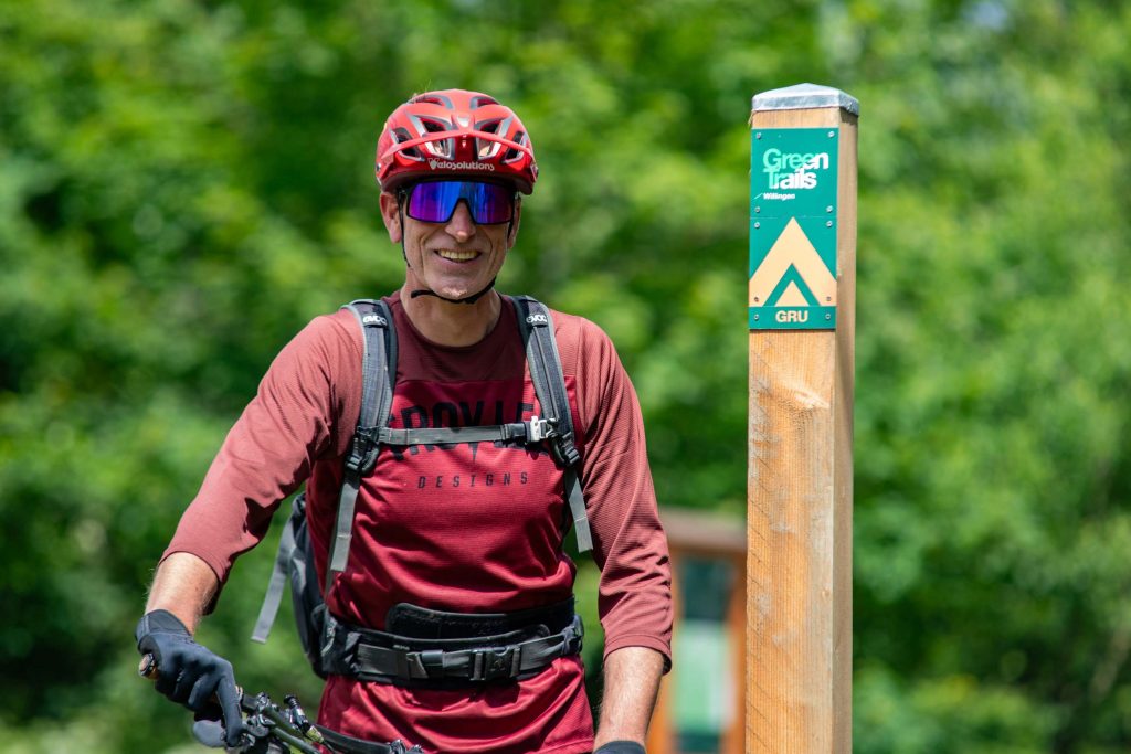 Mann mit Fahrrad, Schutzhelm und Rucksack auf dem Wanderweg neben einem Wegweiser in grüner Natur , Ferienhaus Edersee, Ferienhaus Kellerwald