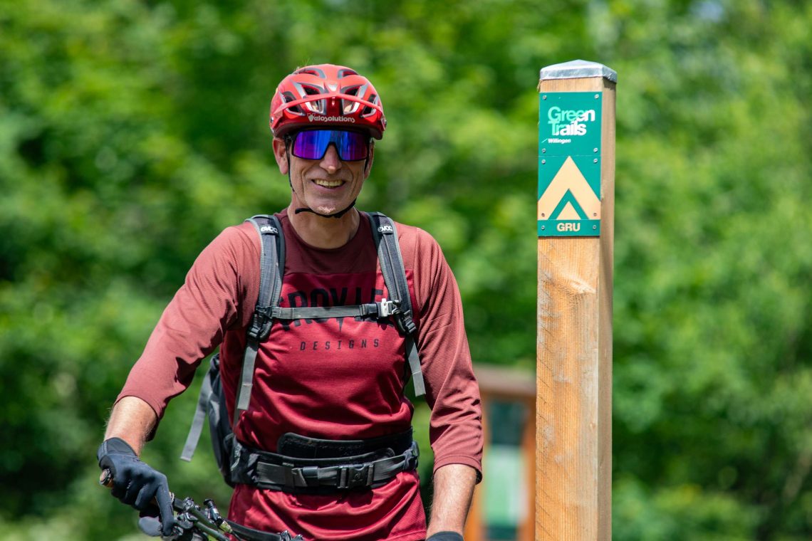 Mann mit Fahrrad, Schutzhelm und Rucksack auf dem Wanderweg neben einem Wegweiser in grüner Natur , Ferienhaus Edersee, Ferienhaus Kellerwald