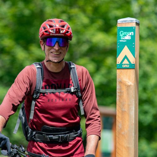 Mann mit Fahrrad, Schutzhelm und Rucksack auf dem Wanderweg neben einem Wegweiser in grüner Natur , Ferienhaus Edersee, Ferienhaus Kellerwald