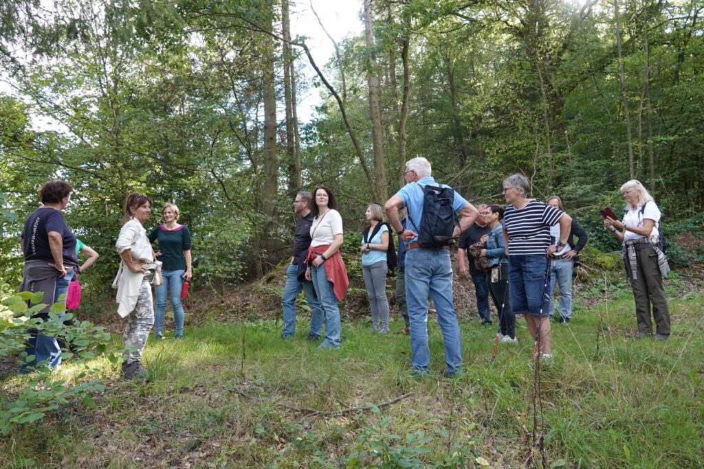 A group of people standing in front of a hiking signpost in the Kellerwald-Edersee National Park listening to a presentation